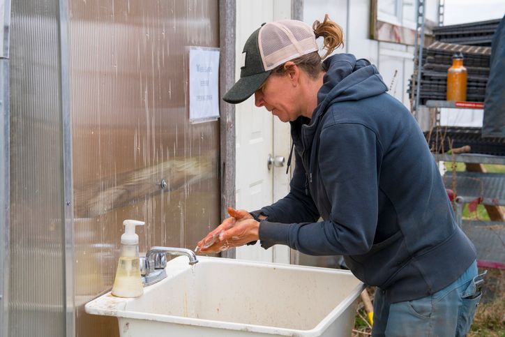Person washing hands at outdoor sink to maintain hygiene