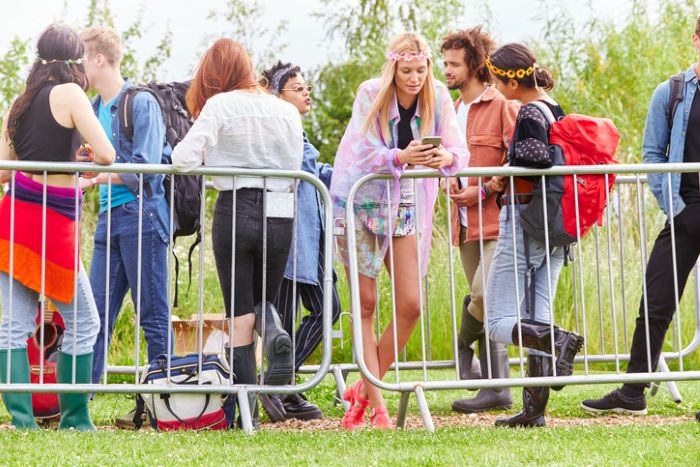 Group of people standing near metal barrier at outdoor music festival checking mobile phones