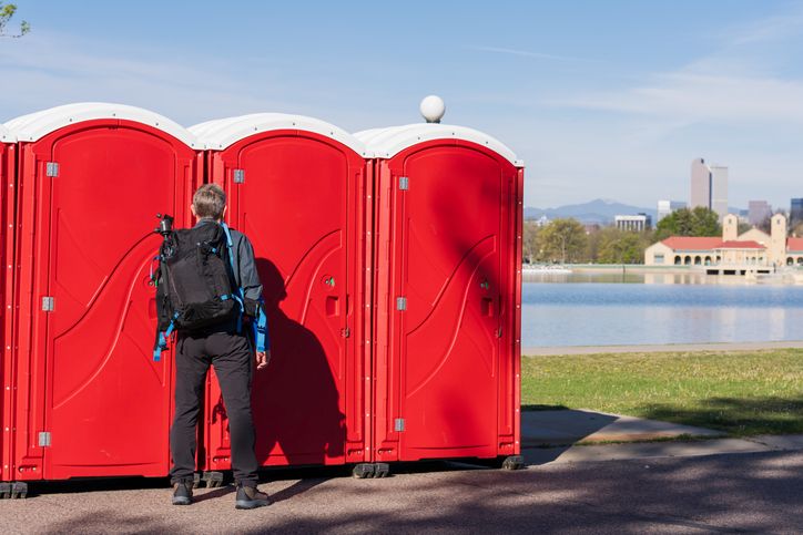 Person standing in front of red portable toilets near lakeside park