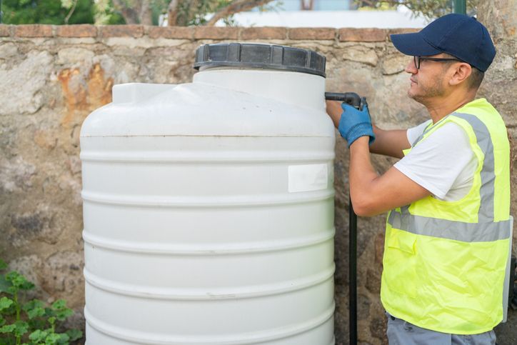Worker connecting pipe to large water storage tank during outdoor maintenance