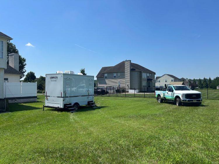 Portable restroom trailer and service truck on grassy residential property in Swedesboro, NJ